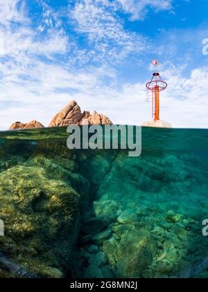 Plan divisé, sur-sous-plan. Vue imprenable sur la moitié du ciel sous-marin avec des rochers et une marque de navigation rouge. Liscia Ruja, Costa Smeralda, Sardaigne. Banque D'Images