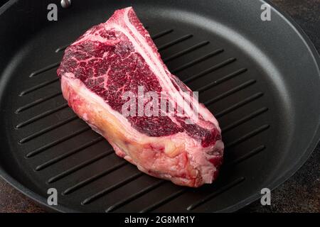 Un steak de club frais, énorme et appétissant, sec et vieux, sur une poêle en fonte, sur un fond rustique sombre Banque D'Images