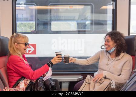 Des femmes heureuses voyageant en train souriant et prenant une tasse de café. Banque D'Images