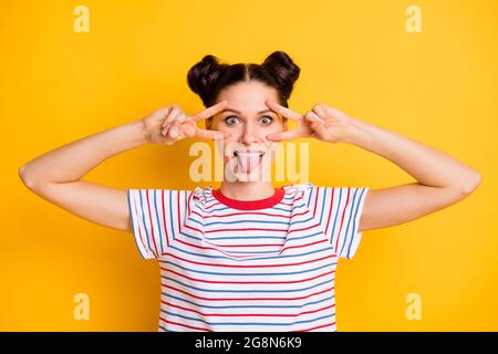 Photo de puéril adorable jeune femme porter un t-shirt rayé montrant la langue V-signes couvrir les yeux isolé couleur jaune fond Banque D'Images