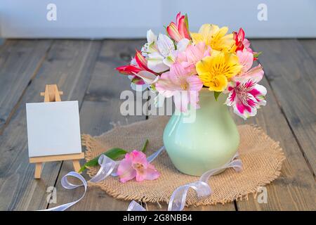 fleurs multicolores dans un vase en argile, molbert vide avec espace de copie sur fond en bois. alstroemeria multicolore, rose, jaune, magenta, blanc an Banque D'Images