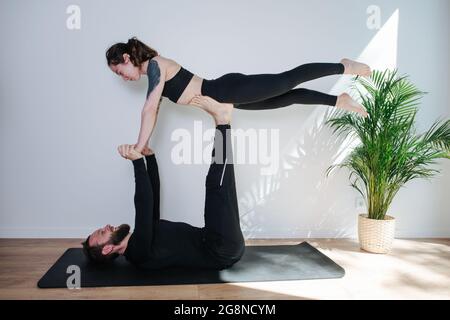 Homme et femme joyeux faisant la forme de gymnastique, il la tient sur les bras et les jambes de strtaight. Ils se sourient les uns les autres, s'amusent. Dans un studio. Banque D'Images