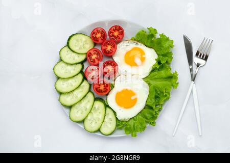 Œufs de poulet frits avec légumes sur une table grise. Concept petit déjeuner. Vue de dessus. Le matin, la nourriture est de base. Tranches de concombres et de tomates fraîches. Plat Banque D'Images