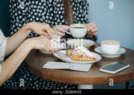 Gros plan sur les femmes qui mangent des croissants et qui boivent du café dans un café. Gros plan, rogné, sans tête. Banque D'Images