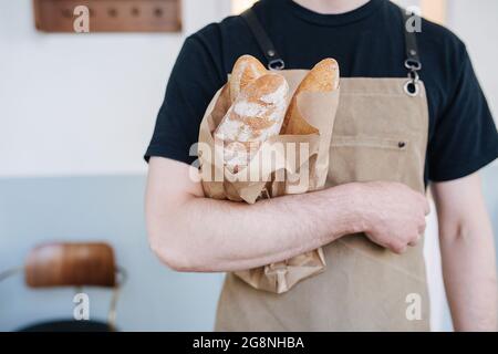 Sac en papier avec baguettes fraîches tenues par un boulanger mâle en tablier beige Banque D'Images