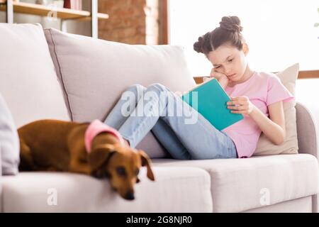 Photo de l'école douce ennuyé fille porter t-shirt rose salon canapé lecture livre dachshund chien intérieur maison chambre Banque D'Images