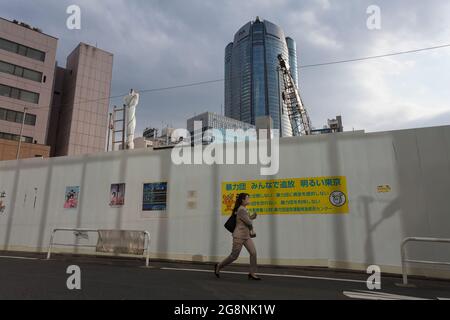 Une employée de bureau, portant un masque facial, marche devant un mur de chantier avec la tour Roppongi Hills derrière, Roppongi, Tokyo, Japon Banque D'Images