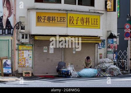 Un sans-abri trie leur collection de matériaux recyclés, qu'ils collectent pour de l'argent, à l'extérieur d'un magasin fermé dans les rues arrière de Shinjuku, Banque D'Images