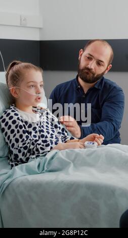 Médecin médecin médecin médecin discutant du traitement de la maladie avec un enfant malade et un père au cours d'un examen médical en salle d'hôpital. Enfant hospitalisé se reposant dans le lit se rétablissant après une chirurgie respiratoire Banque D'Images