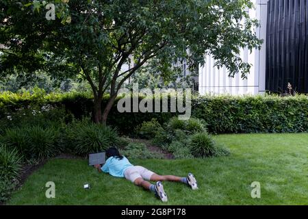 Un jour après la « Journée de la liberté » de Covid, où la distanciation sociale et le port de couvre-visage ne sont plus obligatoires, un homme se trouve sur l'herbe sous des locaux de bureau largement vides, car la majorité des employés de la ville travaillent encore à domicile, le 21 juillet 2021, à Londres, en Angleterre. Banque D'Images