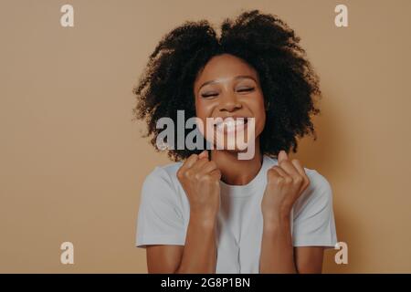 Surjoyée heureux heureux foncé peau jeune femme soulève des poings serrés et sourire Banque D'Images