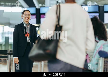 Employé de compagnies aériennes avec écran facial debout à l'aéroport. Un employé de l'aéroport accueille les voyageurs en cas de pandémie. Banque D'Images
