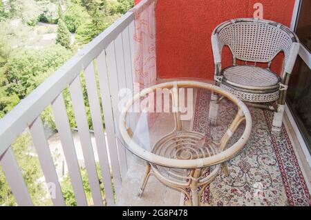 Un coin salon confortable sur le balcon avec une chaise en rotin, une table en verre transparent et un tapis, un concept de loisirs à la maison. Banque D'Images