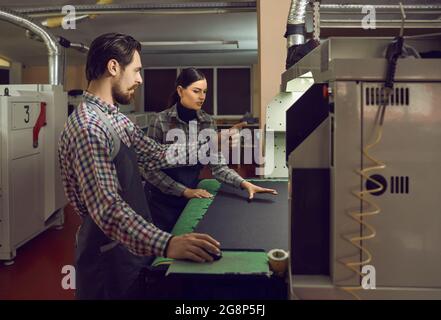 Deux employés d'une usine de chaussures travaillent ensemble avec une machine pour couper le tissu et le cuir. Banque D'Images