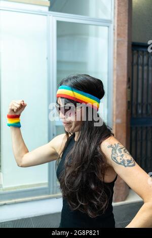 Cool italienne femme avec LGBT poignet et bandeau montrant son muscle sur un fond flou Banque D'Images