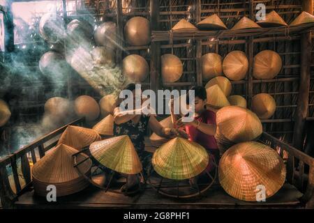 Vietnamienne ancienne femme artisan enseignant le petit-enfant faisant le chapeau traditionnel du vietnam dans l'ancienne maison traditionnelle dans le village AP Thoi Phuoc, Hochi Banque D'Images