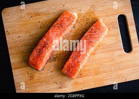 Filets de saumon cru assaisonnés de sel casher et de poivre noir : filets de saumon non cuits sur une planche à découper en bambou nappés de sel et de poivre Banque D'Images