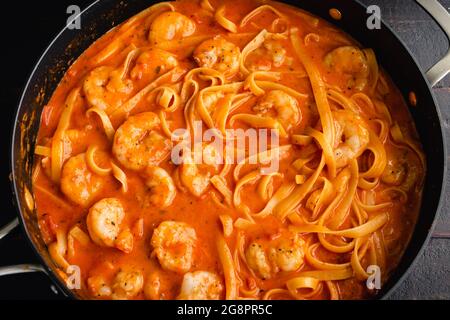 Crevettes et pâtes à la sauce à la crème de tomates dans une sauteuse : une poêle remplie de crevettes et de pâtes de fettucines dans une sauce crémeuse à la tomate Banque D'Images