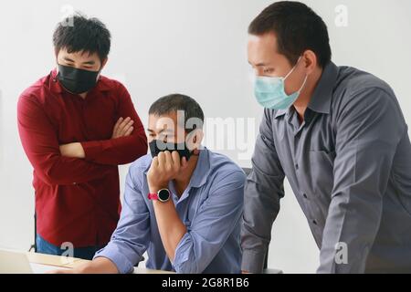 Les hommes d'affaires portant un masque de protection discutent et travaillent ensemble dans la salle de réunion. La pratique sociale à distance prévient le coronavirus COVID-19. Banque D'Images