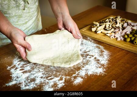 Préparation de la pizza italienne. Pétrissage de la pâte à pain avec des champignons, des olives et du jambon. Banque D'Images