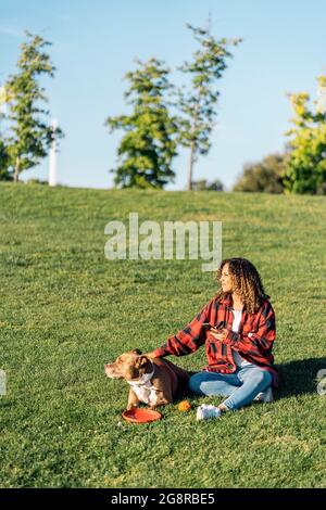 Femme africaine assise dans le parc avec son chien et utilisant son téléphone portable. Banque D'Images