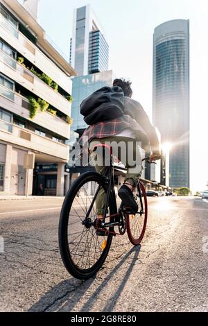 Homme non reconnu avec de longs cheveux et portant un sac à dos à cheval sur son vélo dans la ville. Banque D'Images