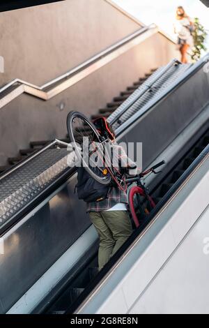 Un boxeur non reconnu transportant son vélo tout en marchant sur les escaliers mécaniques du métro. Banque D'Images