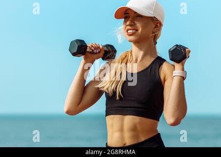 Pleine longueur, bonne santé jeune femme de forme physique, dans les vêtements de sport, faisant des exercices avec des haltères sur la plage, sportive belle jeune femme avec des haltères ou Banque D'Images