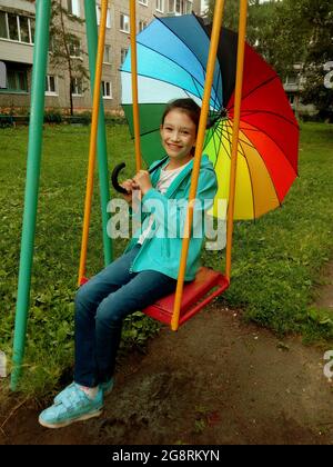 Bonne marche en famille. Un enfant avec un parapluie coloré est assis sur une balançoire. Banque D'Images