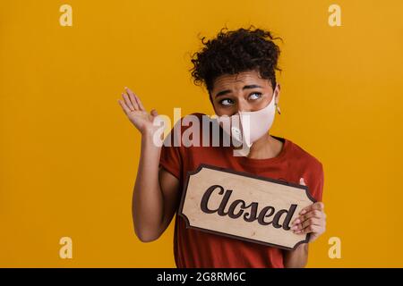 Jeune femme africaine dans un masque de protection médicale montrant un signe fermé sur fond jaune Banque D'Images