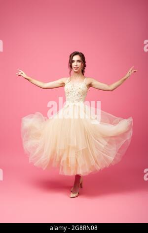 Une jeune femme danse dans une longue robe de balle beige sans manches. Une brunette dans une robe luxuriante avec un corset décoré et des chaussures beiges tourne sur Banque D'Images