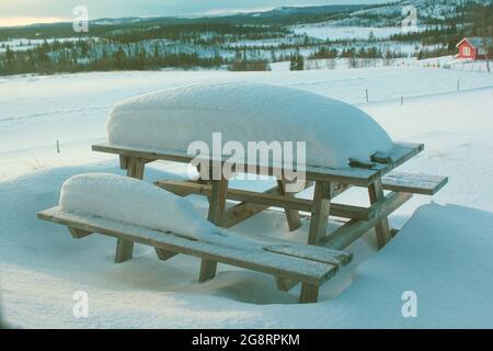 Table de pique-nique enneigée dans le jardin d'une maison de village de montagne au soleil du matin. Le concept de vacances en famille dans les stations de montagne d'EUR Banque D'Images