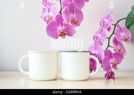 Maquette de deux tasses blanches sur table avec décor de fleurs d'orchidées Banque D'Images