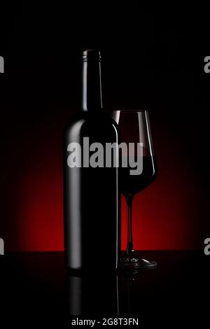 Verre et bouteille de vin rouge sur fond réfléchissant noir et rouge Banque D'Images