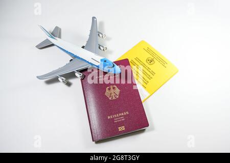 Passeport allemand, certificat international jaune de vaccination et un avion jouet sur fond gris clair, concept pour les exigences de voyage d Banque D'Images