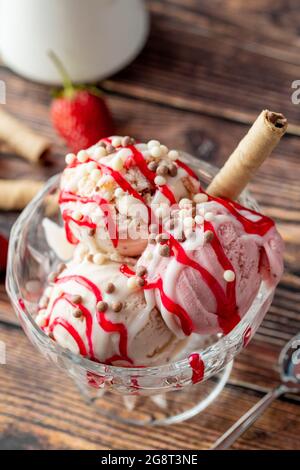 Crème glacée Roma à la fraise, à la banane et à la crème dans un bol en verre avec sauce rouge versée dessus. Banque D'Images