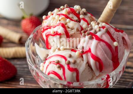 Crème glacée Roma à la fraise, à la banane et à la crème dans un bol en verre avec sauce rouge versée dessus. Banque D'Images
