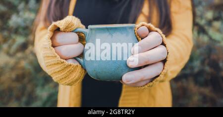 Une jeune femme tient une tasse de thé bleue à l'extérieur Banque D'Images