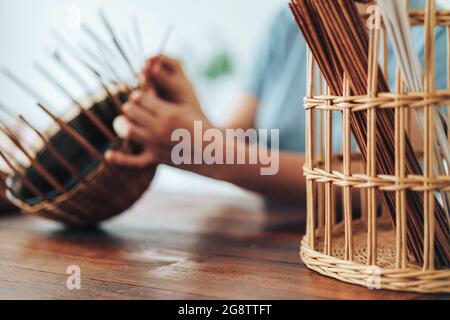 Femme tisse un panier de tubes en papier sur une table en bois. Banque D'Images