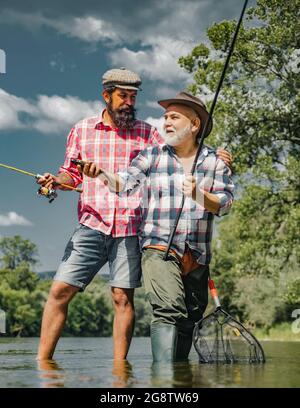 Grand-père et garçon pêchant ensemble. Père et fils heureux de pêche dans la rivière tenant des cannes à pêche. Truite brune. Père et fils de pêche. Banque D'Images