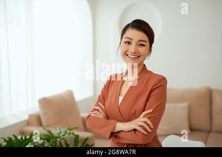 Femme de travail asiatique qui porte un costume noir et des bras croisés dans une salle de bureau blanche, Banque D'Images