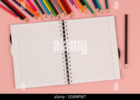 Carnet à carreaux ouvert à l'école et crayons colorés sur fond rose. Livre blanc vierge sur la table. Fournitures de bureau sur le bureau Banque D'Images