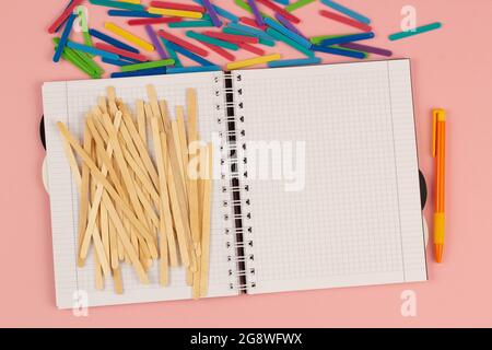 Carnet à carreaux, stylo, popsicle, bâtons de maths colorés sur fond rose. Livre blanc vierge sur la table. Bureau Banque D'Images