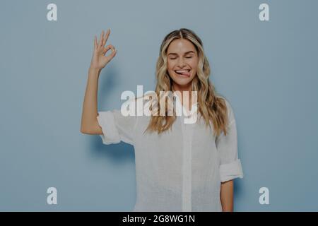 Jeune blonde joyeuse femme caucasienne démontrant l'accord et montrant un geste correct avec les yeux fermés Banque D'Images