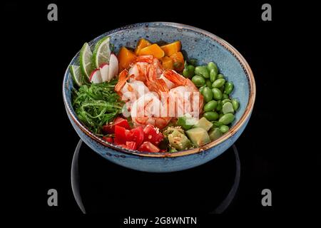 Un bol à poke avec crevettes, mangue, tomates, avocats, haricots édamames, riz, algues wakame, radis et chaux Banque D'Images