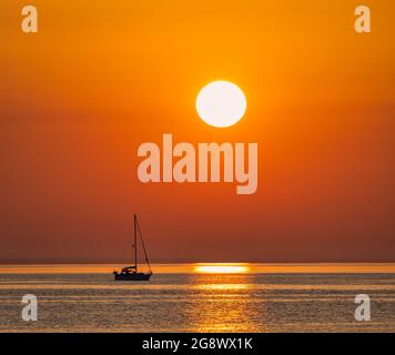 Un petit yacht quitte la marina de Swanage et se dirige vers la Manche avec le soleil levant à l'est Banque D'Images