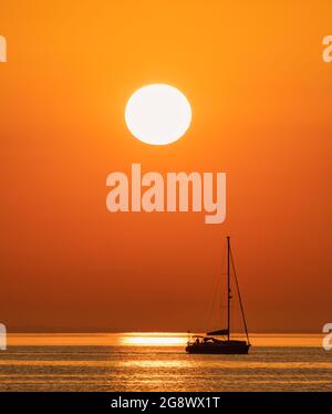 Un petit yacht quitte la marina de Swanage et se dirige vers la Manche avec le soleil levant à l'est Banque D'Images