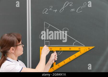 professeur d'école la jeune femme en classe au tableau noir dessine un triangle avec une règle. portrait. gros plan Banque D'Images