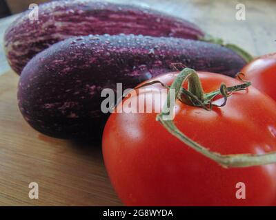 Gros plan d'aubergines avec des tomates sur un panneau de bois rustique Banque D'Images