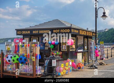 Un kiosque de restauration rapide près de l'entrée d'une plage avec des jouets de plage colorés exposés. Un ciel avec des nuages est au-dessus. Banque D'Images